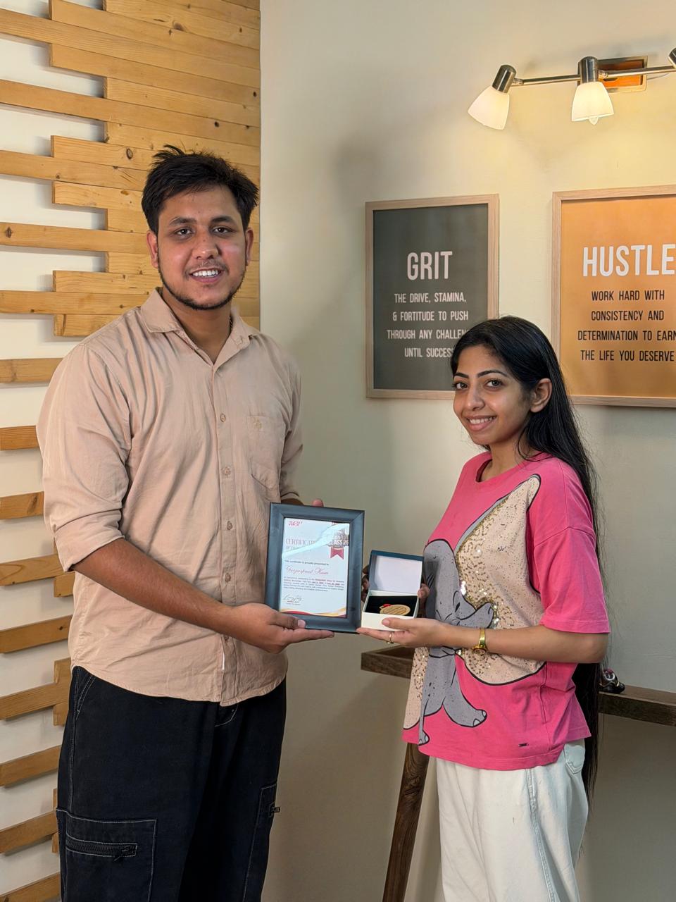 Graduate receiving her certificate in front of the Grit and Hustle wall
